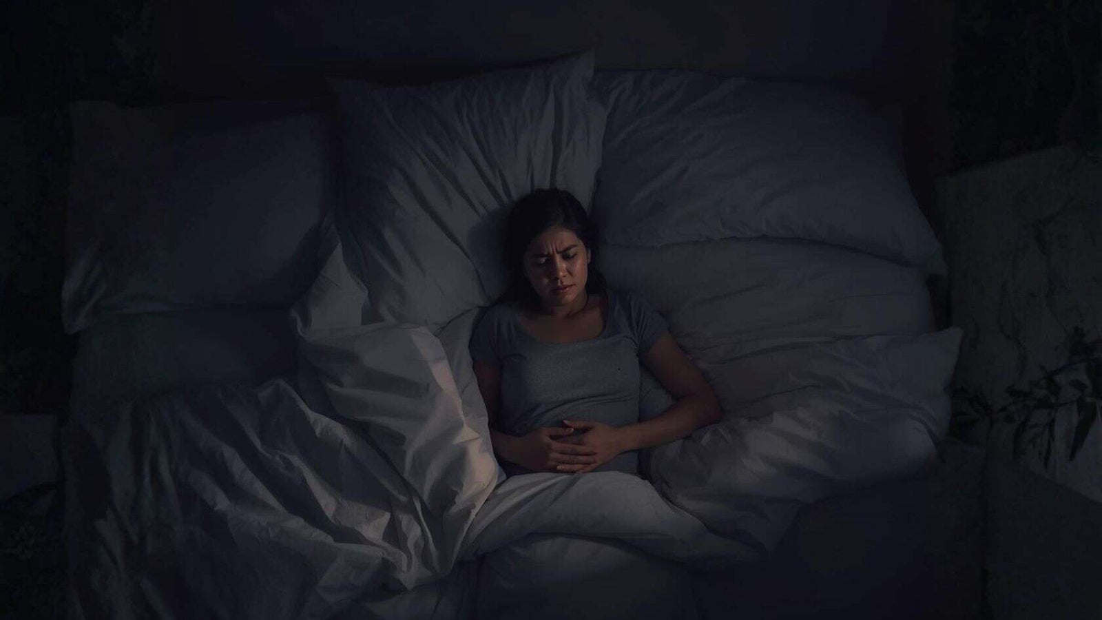 woman in bed holding her stomach experiencing pms symptoms  Apotheka Herbal